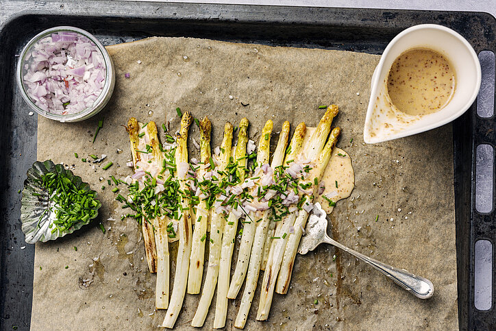 Bakplaat met witte asperges met rode ui en groene kruiden, kommetje moaterdsaus