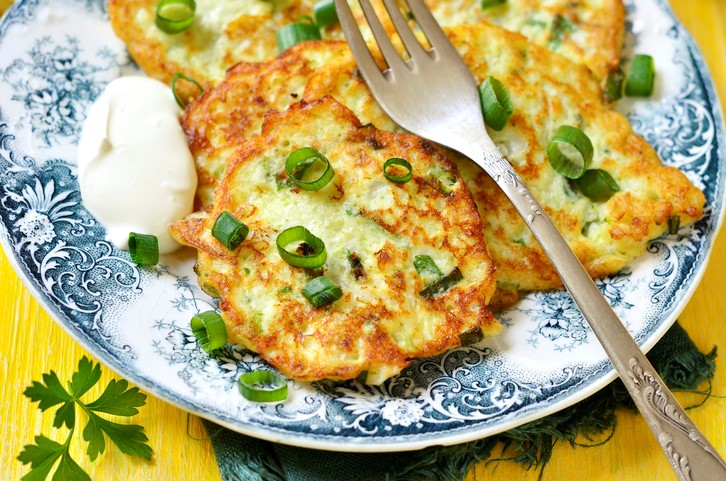 Kleine bloemkoolpannenkoekjes met stukjesbosuitjes en een flinke schep cremefraiche op een blauwwit bord