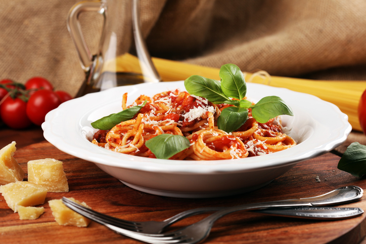 Bord pasta met tomatensaus, blaadjes basilicum. Naast het bord stukjes kaas
