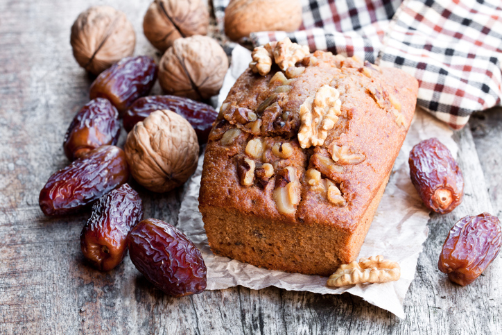 Cake met daarop walnoten, dadels en walnoten in bast op een houten tafel met een geruite doek