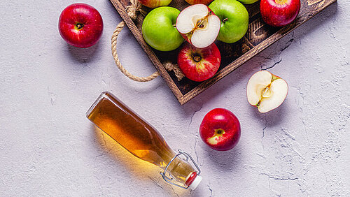Hoe maak je appelazijn? Houten dienblad met appels en liggend een flesje appelazijn