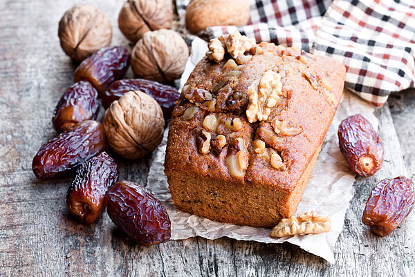 Cake met daarop walnoten, dadels en walnoten in bast op een houten tafel met een geruite doek