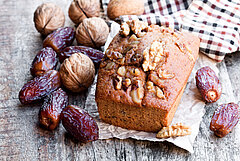 Cake met daarop walnoten, dadels en walnoten in bast op een houten tafel met een geruite doek