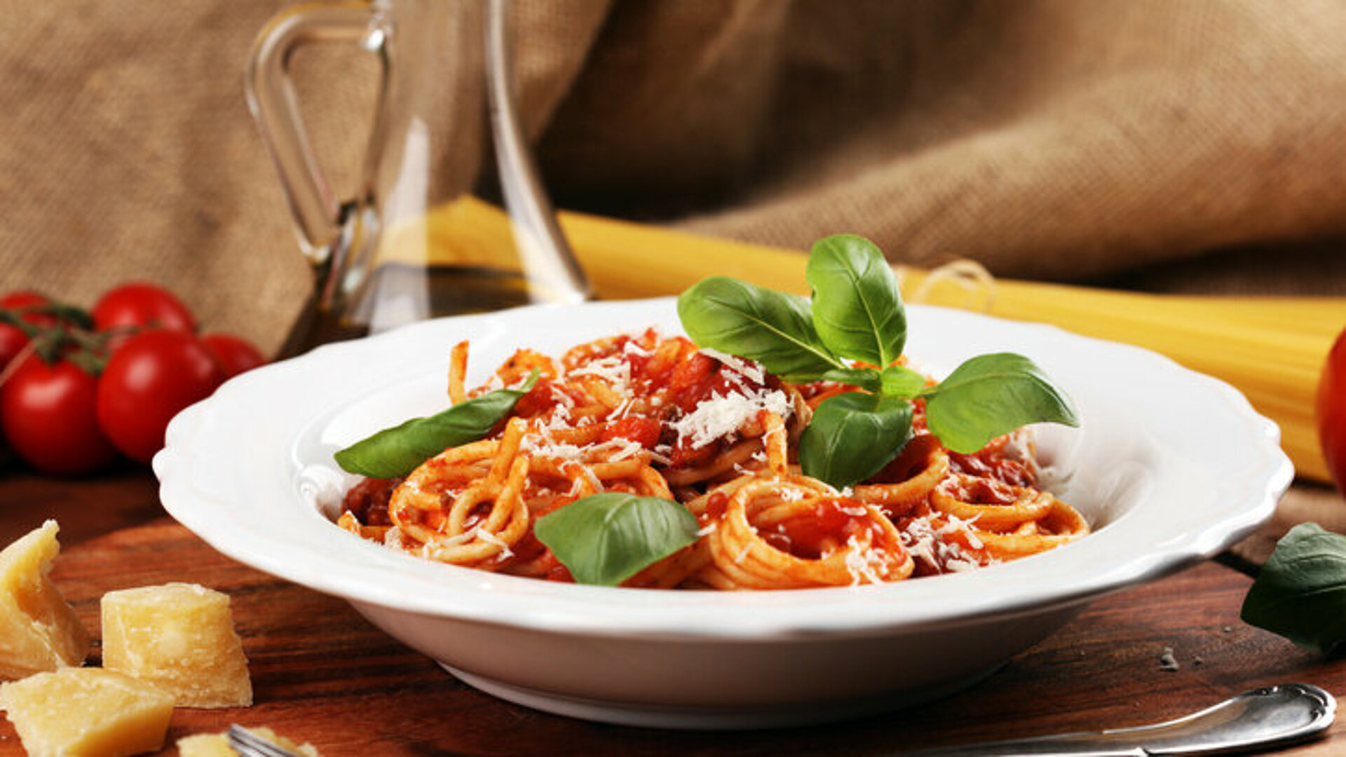Bord pasta met tomatensaus, blaadjes basilicum. Naast het bord stukjes kaas