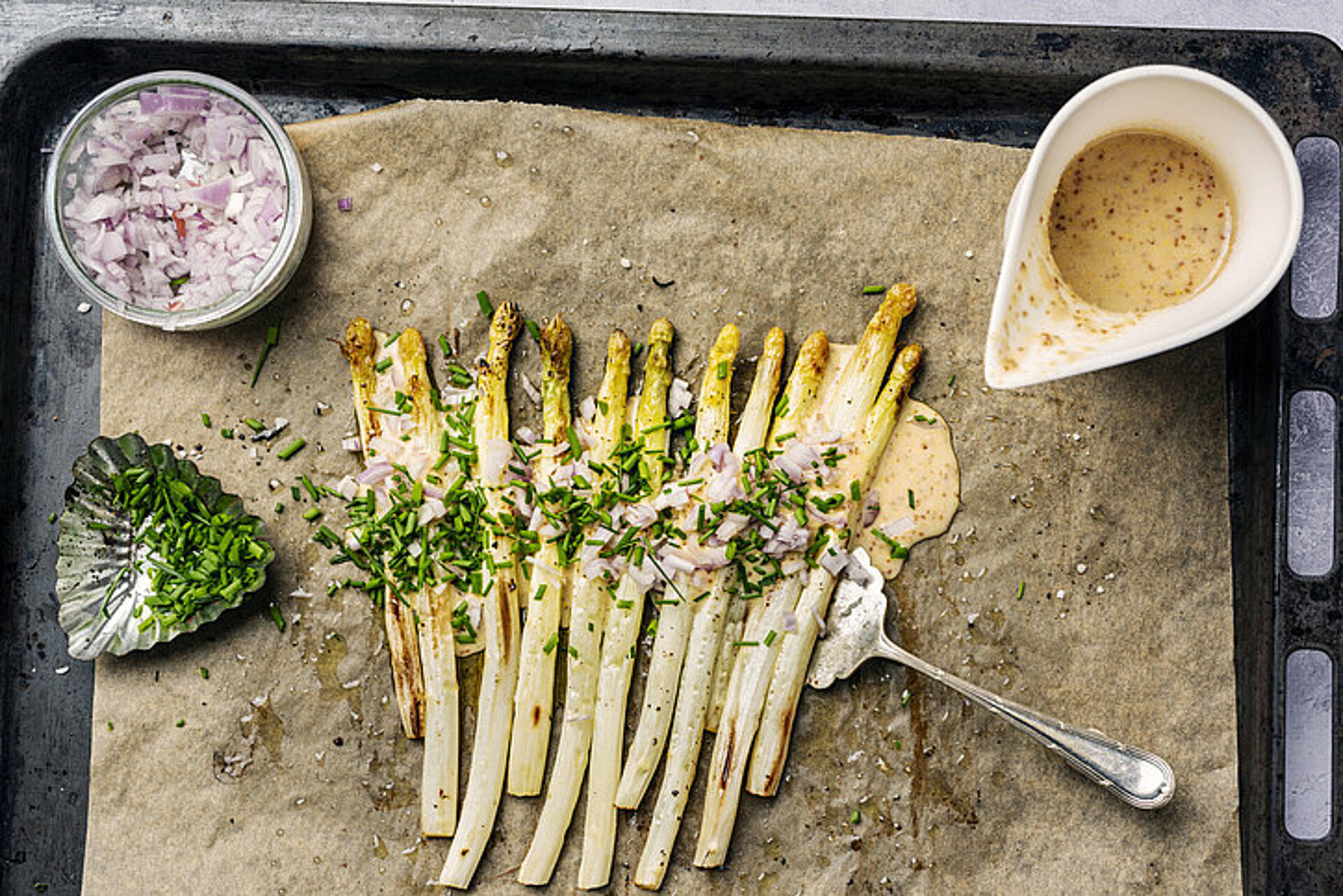 Asperges van de bakplaat Bakplaat met witte asperges met rode ui en groene kruiden, kommetje moaterdsaus