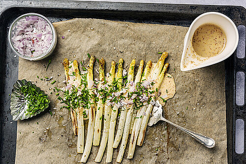 Bakplaat met witte asperges met rode ui en groene kruiden, kommetje moaterdsaus