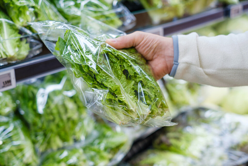 Wat is gezonder? Verse sla of sla uit een zakje? Een hand van een persoon pakt een zak sla uit een koelvitrine
