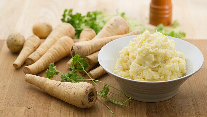 puree van pastinaak in een schaal met hele pastinaken op de achtergrond
