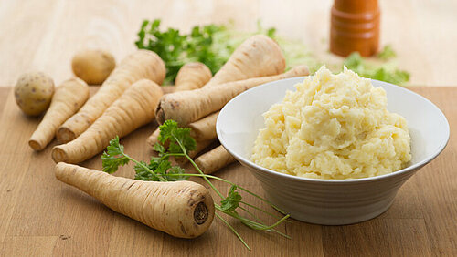 puree van pastinaak in een schaal met hele pastinaken op de achtergrond