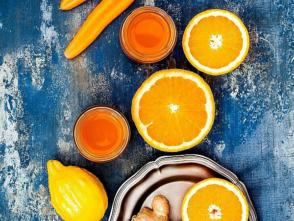 wottel, sinaasappel en gember op een tafel met een glas smoothie erbij