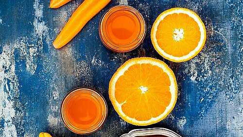 wottel, sinaasappel en gember op een tafel met een glas smoothie erbij