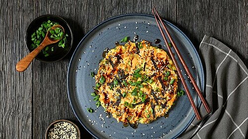 Bord met een met groenten gevulde pannenkoek op een donkeler Japans uitziende) tafel