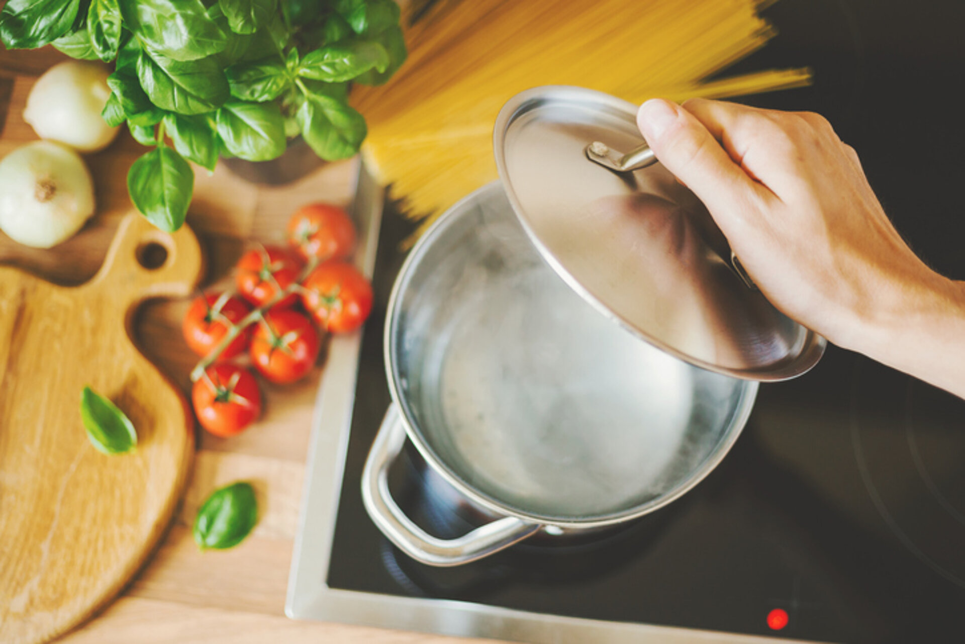 koken met deksel op de pan naast een plank met tomaten en kruiden