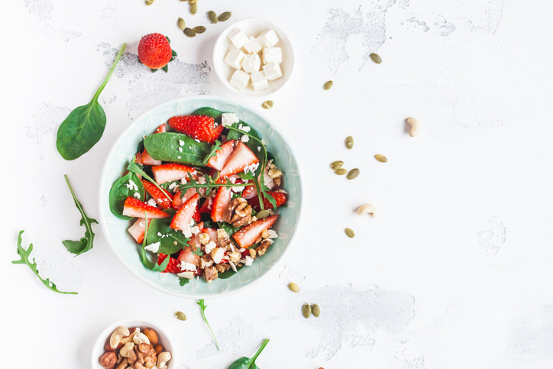Diep wit bord met een salade van aardbeien, groene salade noten en pitten met om het bord wat losse ingredienten