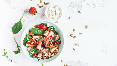 Lentesalade met spinazie en aardbeien Diep wit bord met een salade van aardbeien, groene salade noten en pitten met om het bord wat losse ingredienten