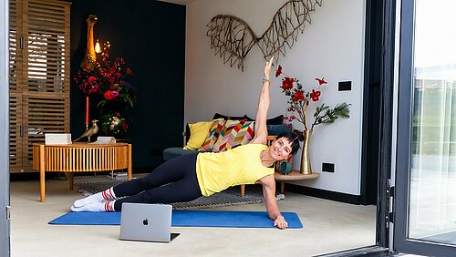 Vrouw volgt online sportles en sport in woonkamer op yogamatje