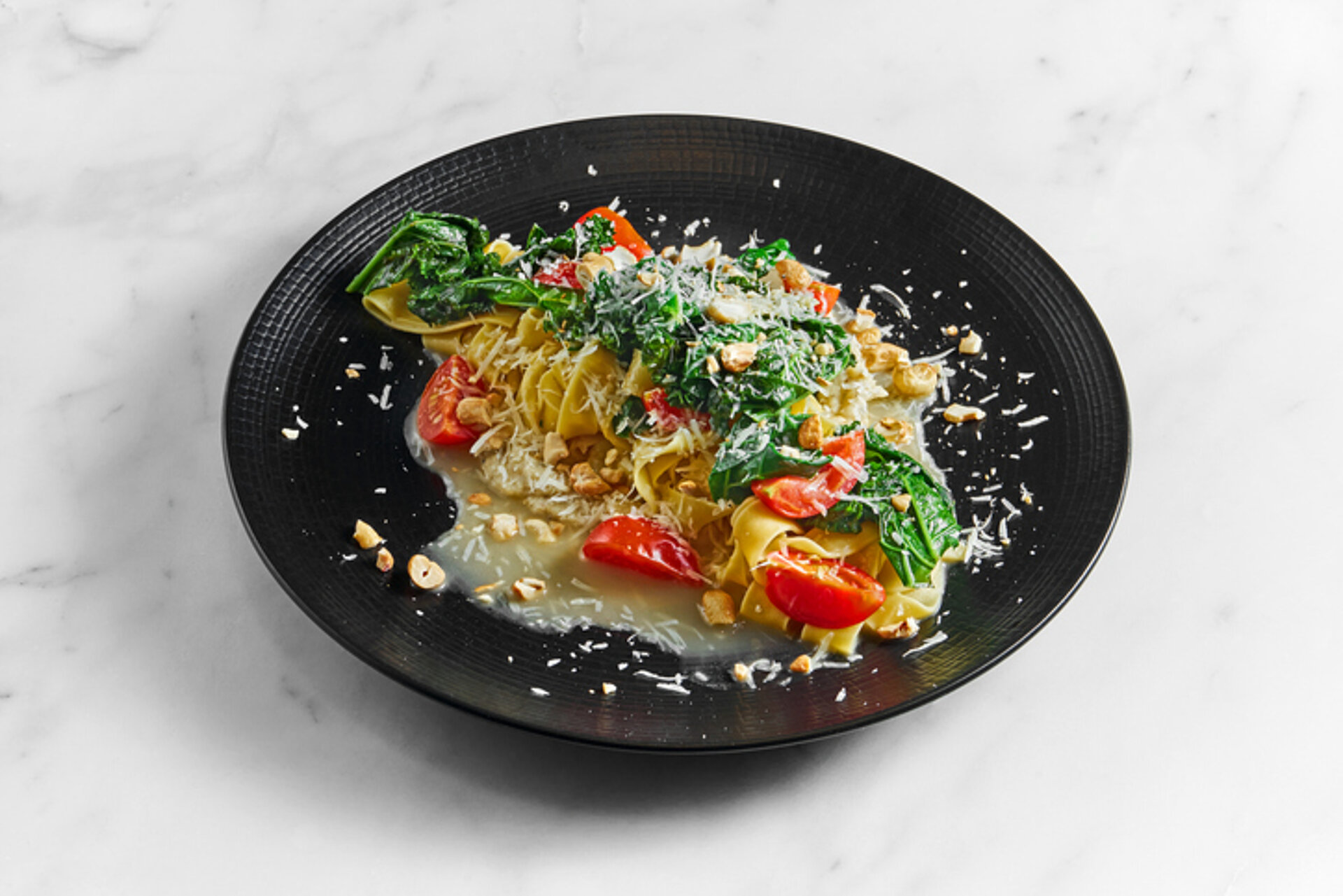 Koekenpan met daarin parpadelle tomaten, pastinaak en spinazie, bestrooid met Parmezaanse kaas