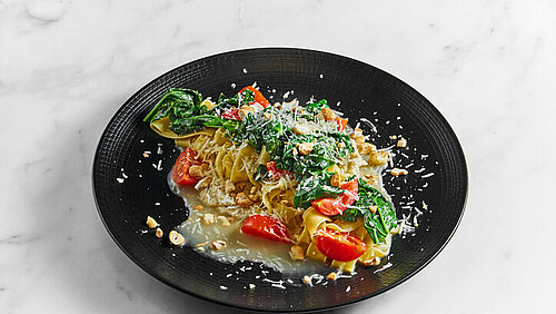 Koekenpan met daarin parpadelle tomaten, pastinaak en spinazie, bestrooid met Parmezaanse kaas