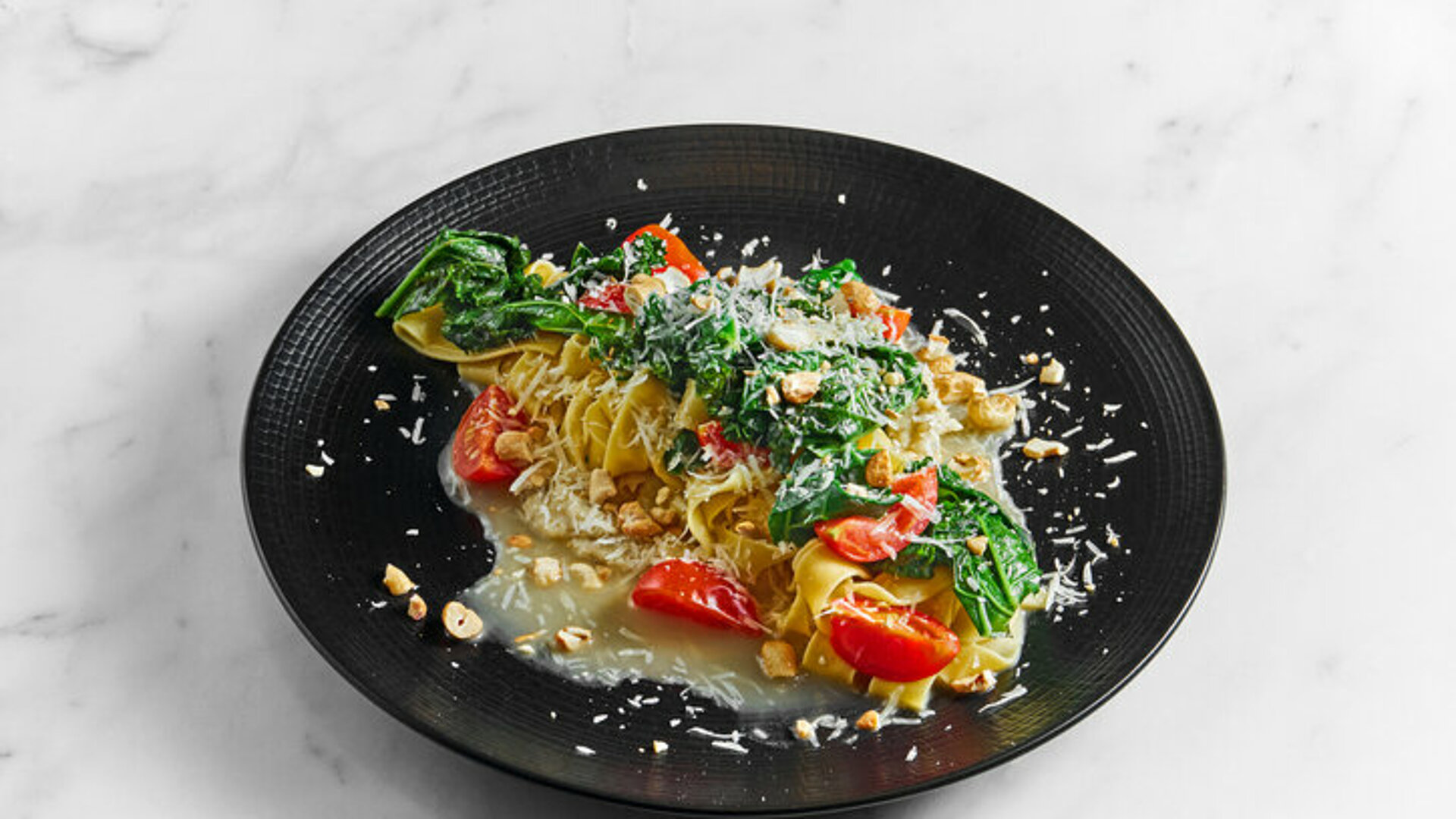 Koekenpan met daarin parpadelle tomaten, pastinaak en spinazie, bestrooid met Parmezaanse kaas