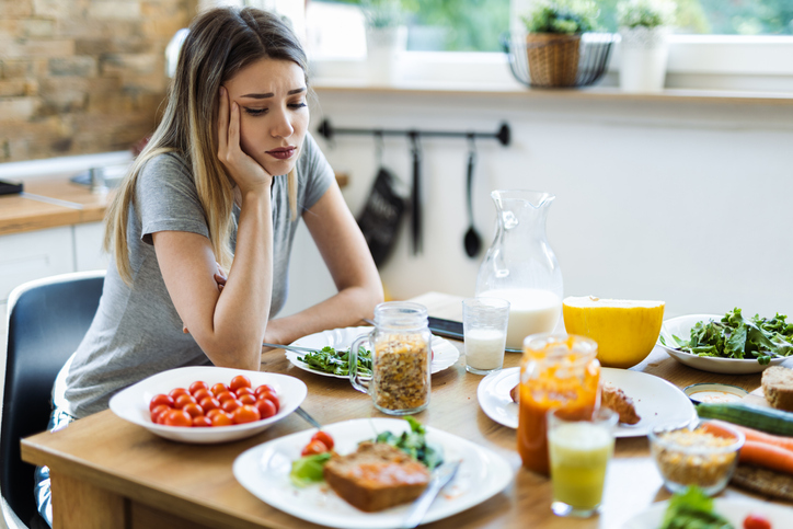 Vrouw met laag gewicht zittend aan een tafel vol eten